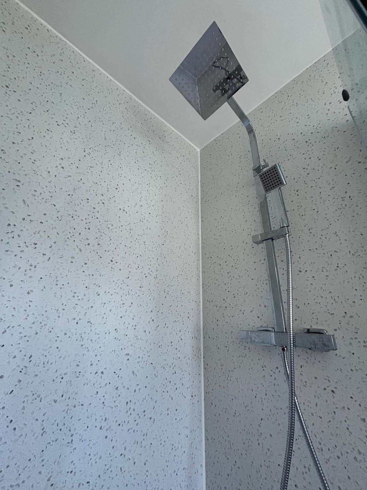 Chrome rainfall shower and handheld shower fitted to speckled wall panels
